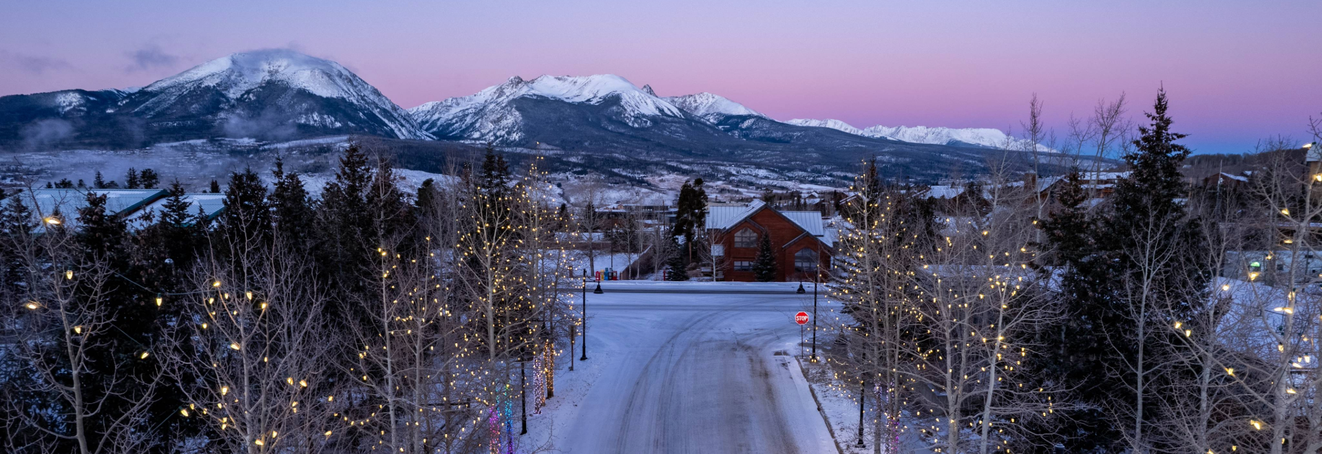 A picturesque snowy road featuring glowing lights, with stunning mountains visible in the distance.