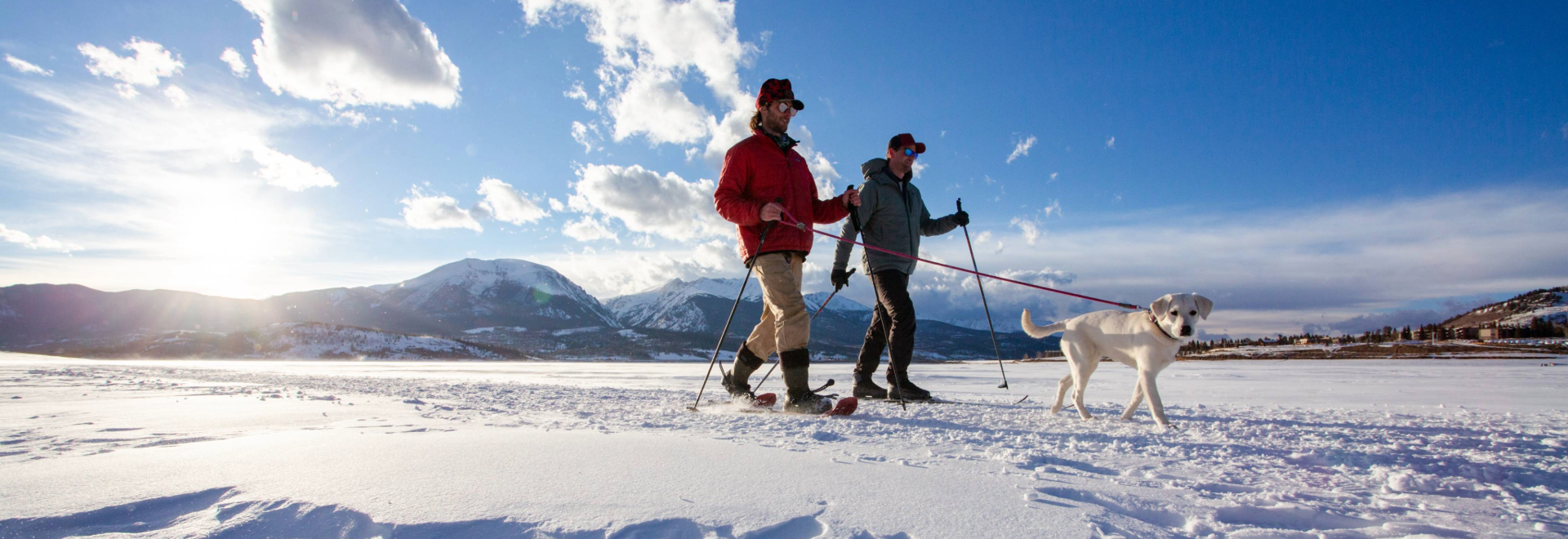 Two individuals stroll through the snow, accompanied by their dog, enjoying a winter day outdoors.